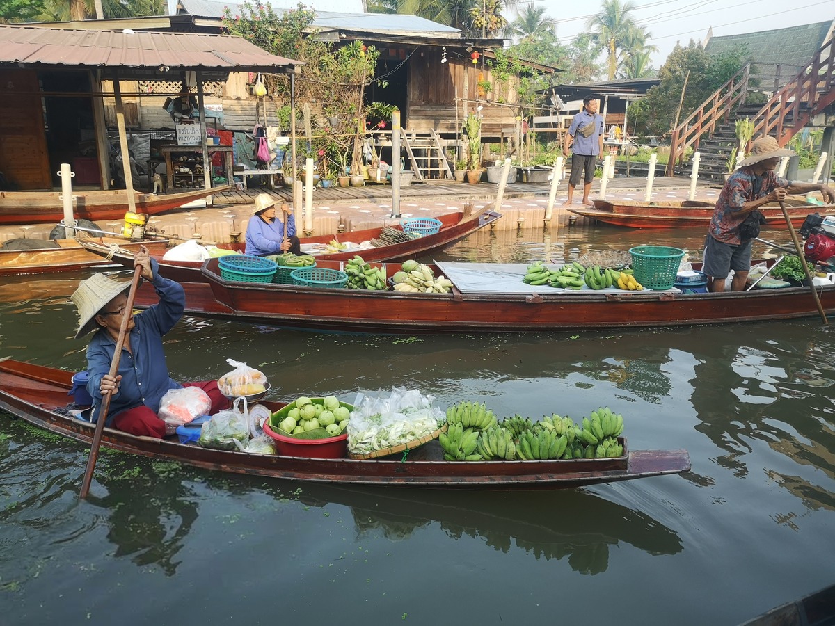 Vendeuse pagayant sur un marché flottant, au milieu de barques chargées de bananes et de fruits
